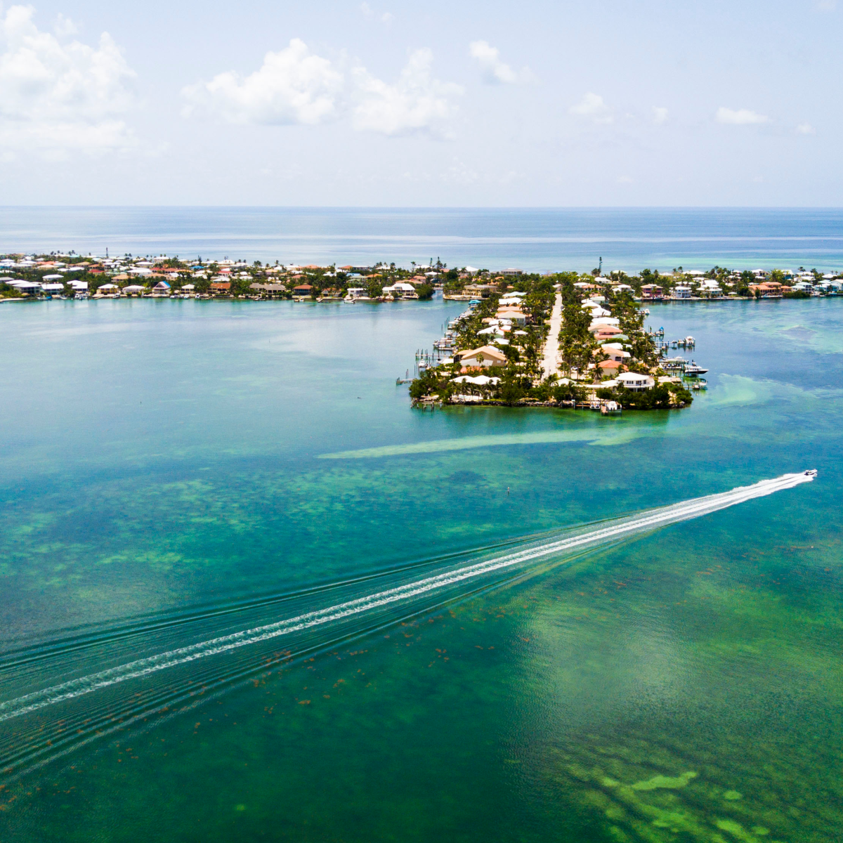 Aerial view of a coastal town with a boat creating a wake on the turquoise water.