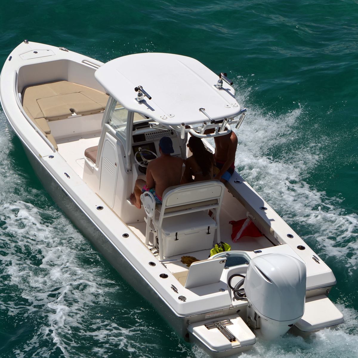 A white motorboat with people onboard cruising through clear blue water.